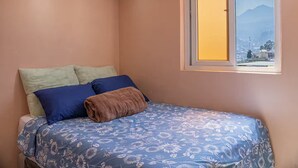 Un dormitorio con cama, almohadas, una ventana y vista a la montaña.