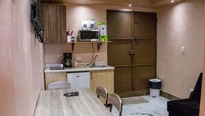 Una cocina compacta con microondas, cafetera y refrigerador pequeño. Hay una mesa de comedor con sillas y un control remoto encima.