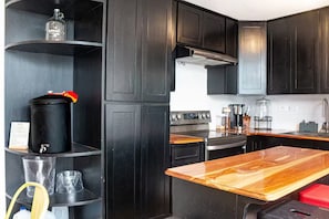 A modern kitchen with black cabinets, a wooden countertop, a stove, and a coffee maker. - Hermosa casa colonial en Antigua Guatemala (Alotenango)