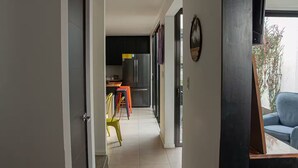 Kapea käytävä johtaa modernilla laitteistolla varustettuun keittiöön, värikkäillä tuoleilla sisustettuun ruokailutilaan, josta on näkymä ulos.