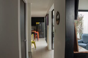 Un corridoio stretto che porta a una cucina con elettrodomestici moderni, una sala da pranzo con sedie colorate e vista sull'esterno.