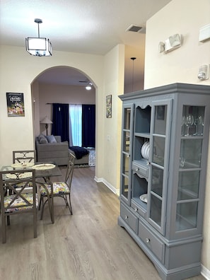 A dining area with a glass-top table, chairs with patterned cushions, a gray cabinet with glass doors, and a ceiling light fixture.
