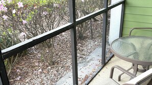 Un espace patio avec une table et des chaises en verre, une vue sur un jardin agrémenté d’arbustes en fleurs et un mur végétal.