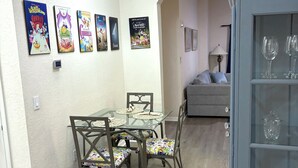 Un espace repas avec une table et des chaises en verre, un lustre et des œuvres d’art murales.