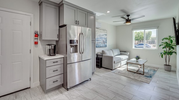 A modern kitchen with a stainless steel refrigerator, grey cabinets, and a ceiling fan. - Cozy Coachella Valley Home! Golf, Shop + Dine (Indio)