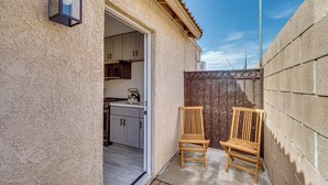 A small patio area with two wooden chairs, a metal gate, and a kitchen visible through an open door. - Cozy Coachella Valley Home! Golf, Shop + Dine (Indio)