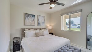 A bedroom with a bed, a nightstand, a lamp, a ceiling fan, and a window with a view of the outside. - Cozy Coachella Valley Home! Golf, Shop + Dine (Indio)
