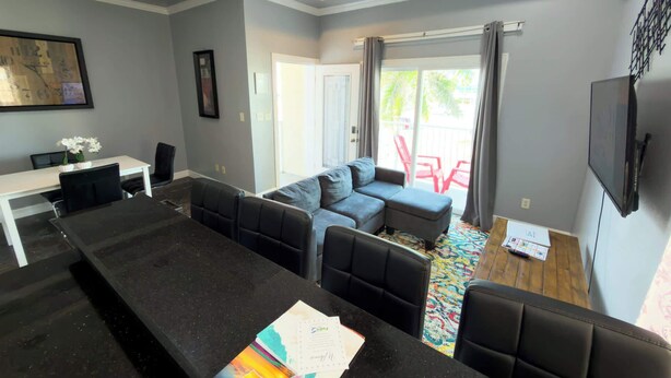 A modern living room with a black sofa set, a dining table with chairs, and a TV mounted on the wall. - Steps to the Beach Great Value Pool Home (South Padre Island)