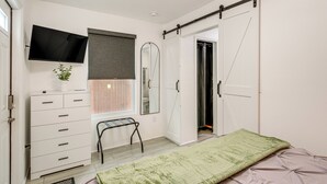 Ein Schlafzimmer mit einem Bett, einem Schminktisch, einem Fernseher, einem Spiegel und einer Schiebetür.