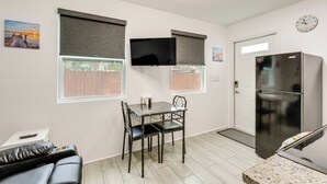 Eine kompakte Küche mit Esstisch, Stühlen, einem Kühlschrank und einem an der Wand befestigten Fernseher.
