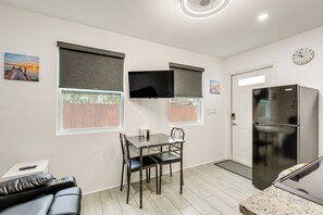 Eine kompakte Küche mit Esstisch, Stühlen, einem Kühlschrank und einem an der Wand befestigten Fernseher.