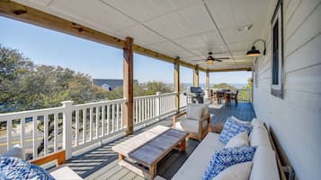 Una terraza techada con mobiliario exterior, un ventilador de techo y vista al océano.