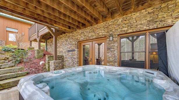 Un bain à remous dans un espace extérieur entouré de murs en pierre, avec des poutres en bois au-dessus.