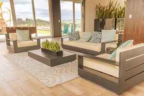 Ein moderner Außenbereich mit Sofas, Couchtischen, großen Fenstern und Blick ins Grüne.