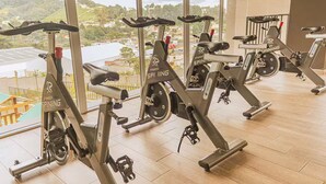 Række stillestående cykler i et fitnesscenter med store vinduer med udsigt over et naturskønt landskab.