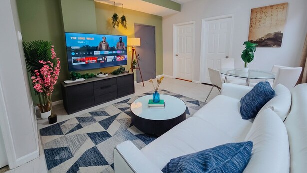 Ein modernes Wohnzimmer mit Fernseher, einem weißen Sofa, einem runden Couchtisch und einem gemusterten Teppich.