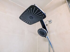 Eine Dusche mit einem eckigen und einem runden Duschkopf, beide mit mehreren Löchern, in einem gefliesten Badezimmer.