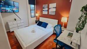 Ein Hotelzimmer mit Bett, Schreibtisch, Stuhl, Fernseher, Kommode und Pflanze.