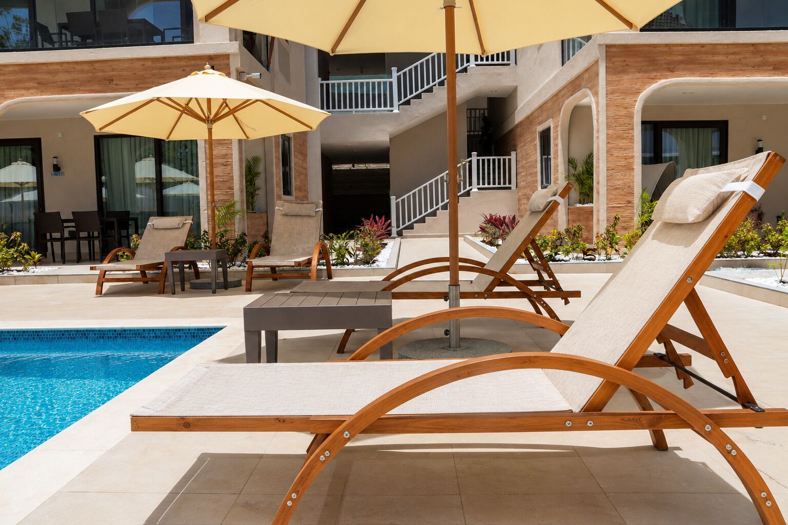 A poolside area with lounge chairs, umbrellas, and a staircase leading to an upper level.