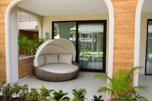 Un espacio de asiento circular y acolchado, con toldo, rodeado de plantas y vista a un edificio a través de un ventanal.