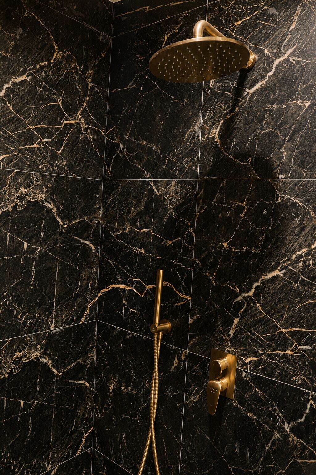 A showerhead and control panel on a black marble wall.