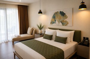Quarto de hotel com cama, mesas de cabeceira, escrivaninha, cadeira, janela com cortinas e obras de arte na parede.