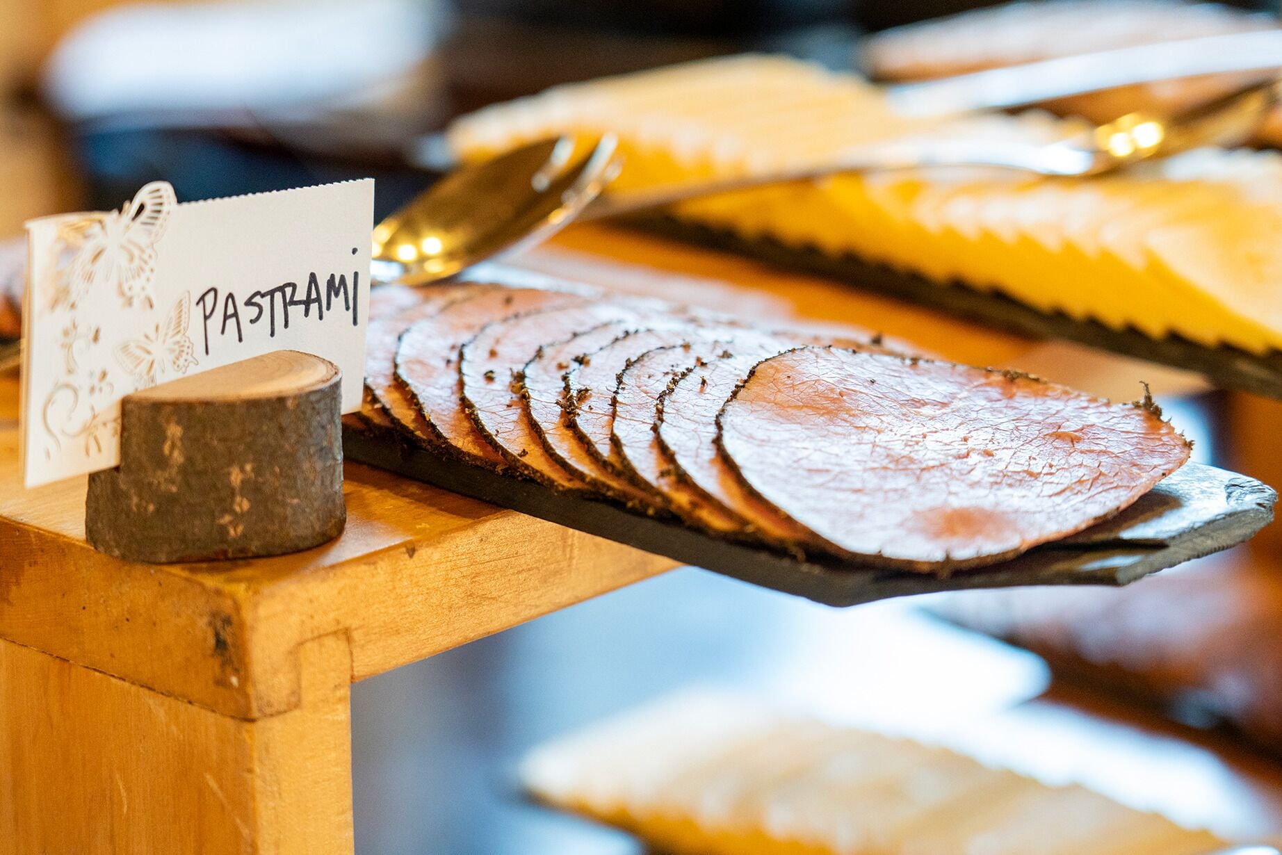Una tabla de madera con carne en rodajas, un letrero que dice 'PASTAM' y una taza pequeña.