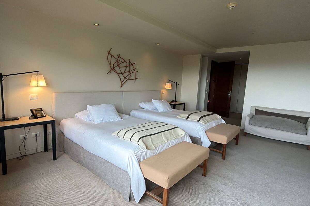 Ein Hotelzimmer mit zwei Betten, Nachttischen, einer Lampe, einem Sofa und einem Wandbild.