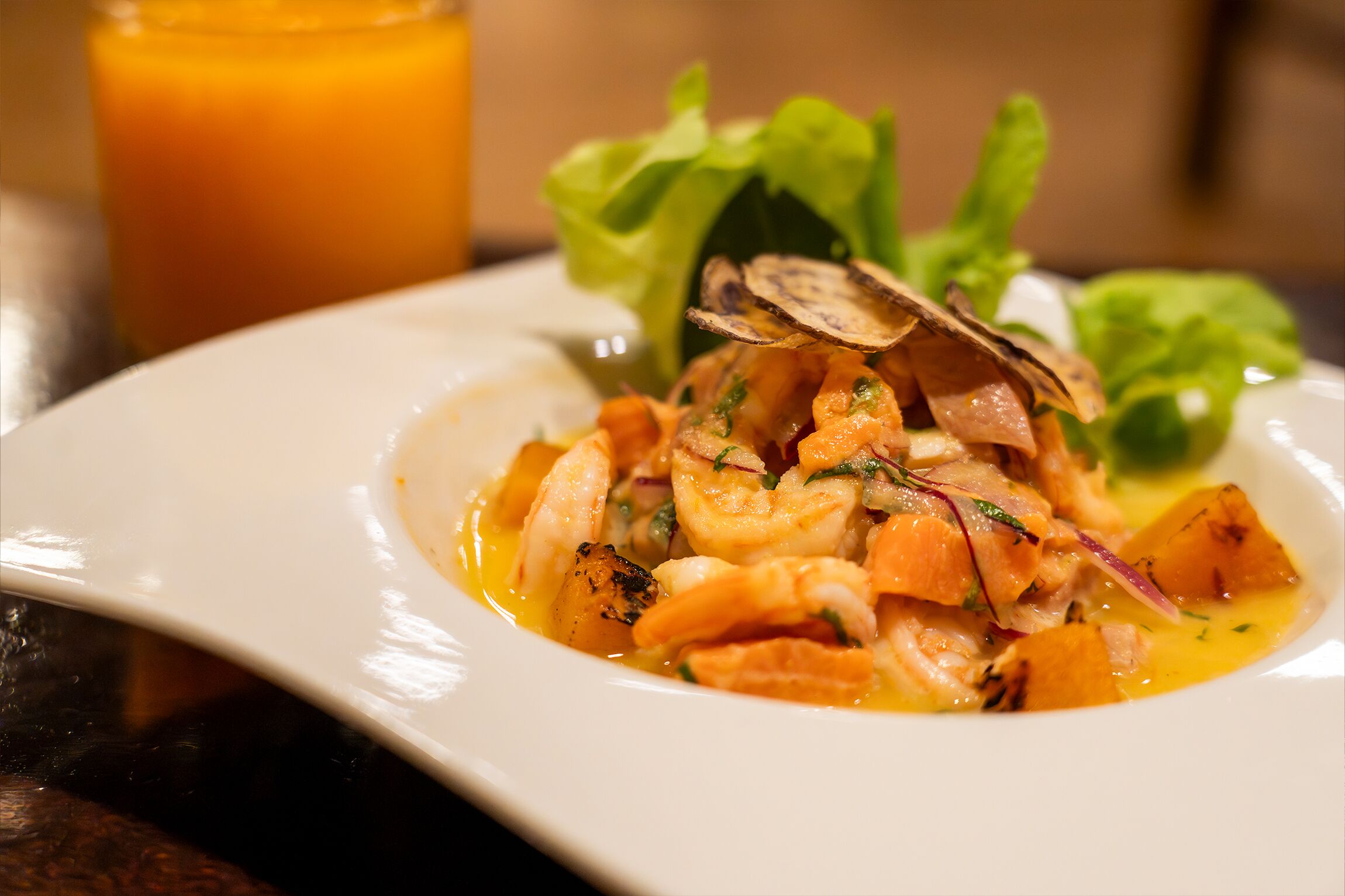 A plate of food with shrimp and vegetables, accompanied by a glass of orange juice.