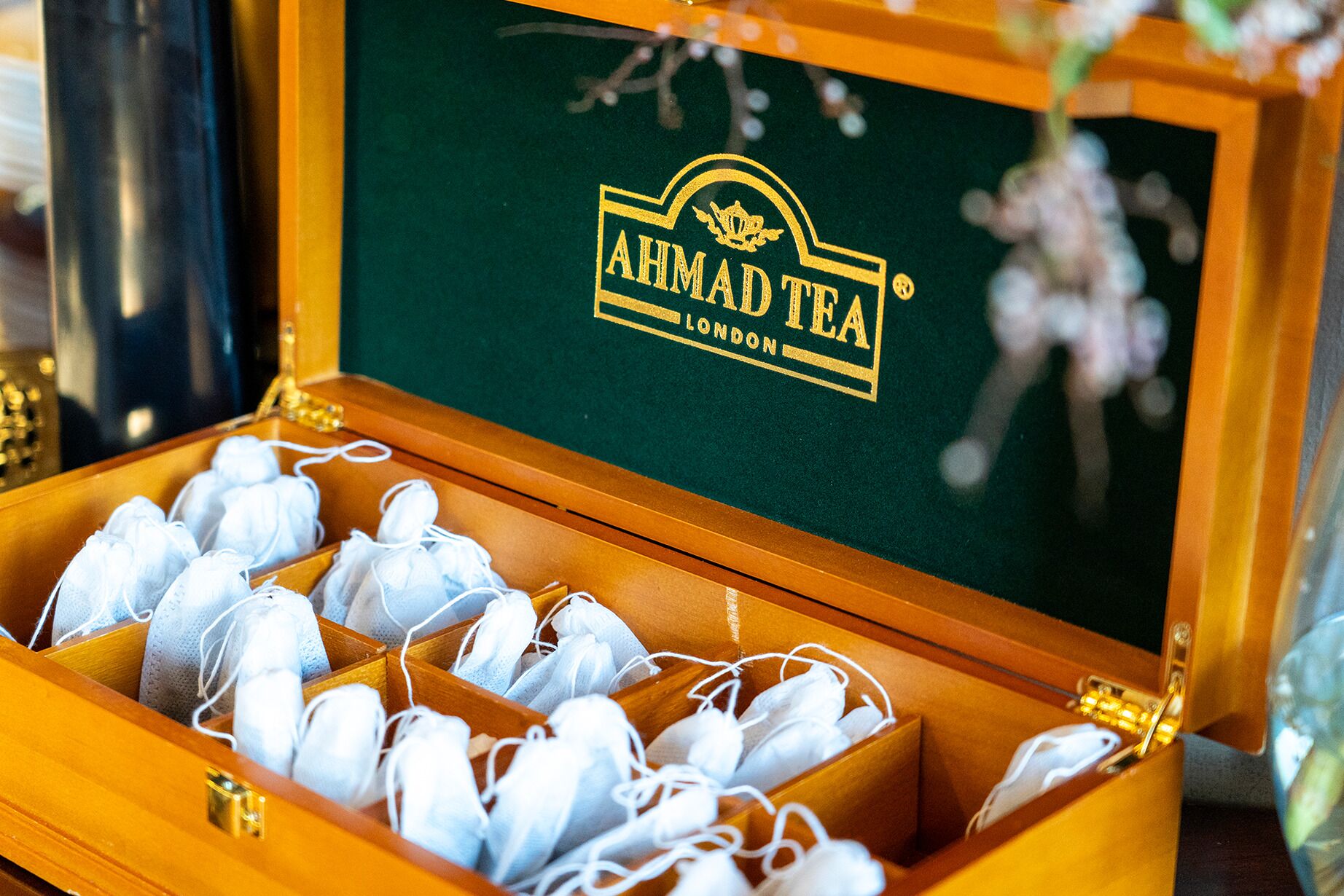 Puinen laatikko, jonka sisäpuoli on vihreä ja jonka kannessa on logo «AHMAD TEA LONDON». Laatikon sisällä on useita valkoisia kasvonaamioita.