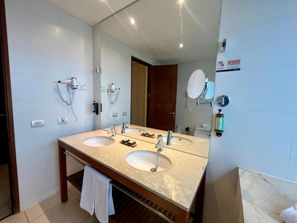 A bathroom with two sinks, a large mirror, and a hairdryer on the wall.