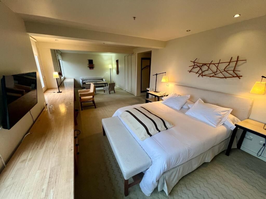 Una habitación de hotel con una cama grande, mesitas de noche, un escritorio y un televisor.