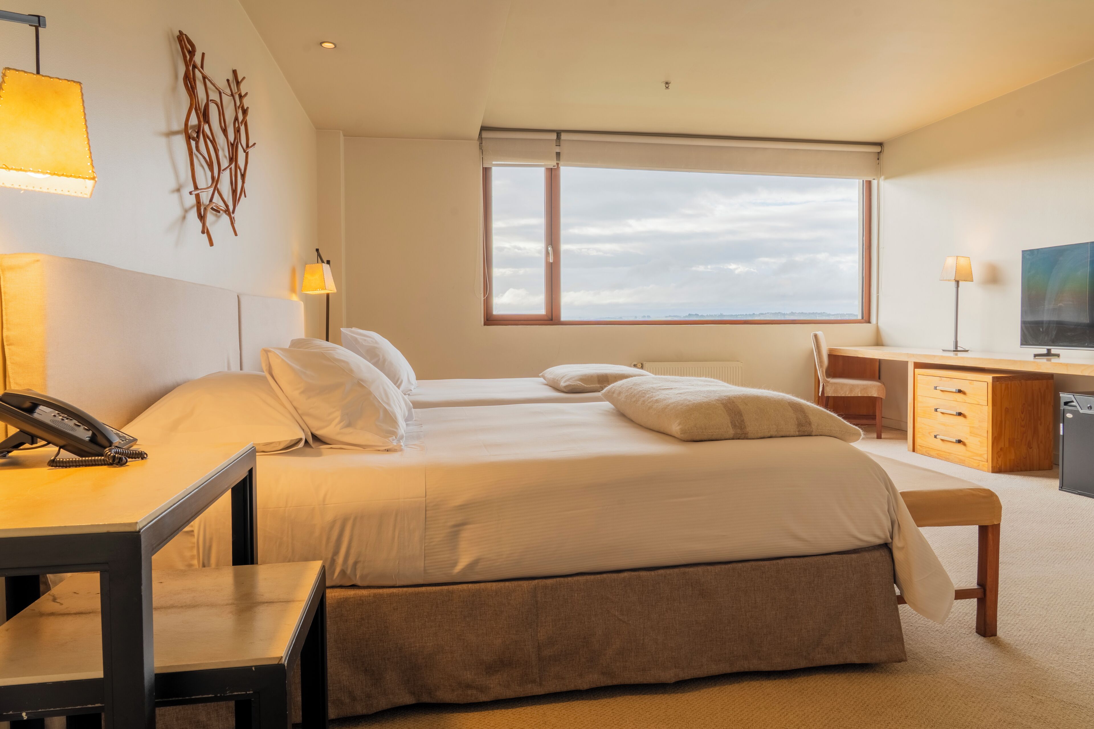 Ein Hotelzimmer mit einem Bett, Nachttischen, einem Schreibtisch, einem Sessel, einem Fernseher und einem Fenster mit Blick.