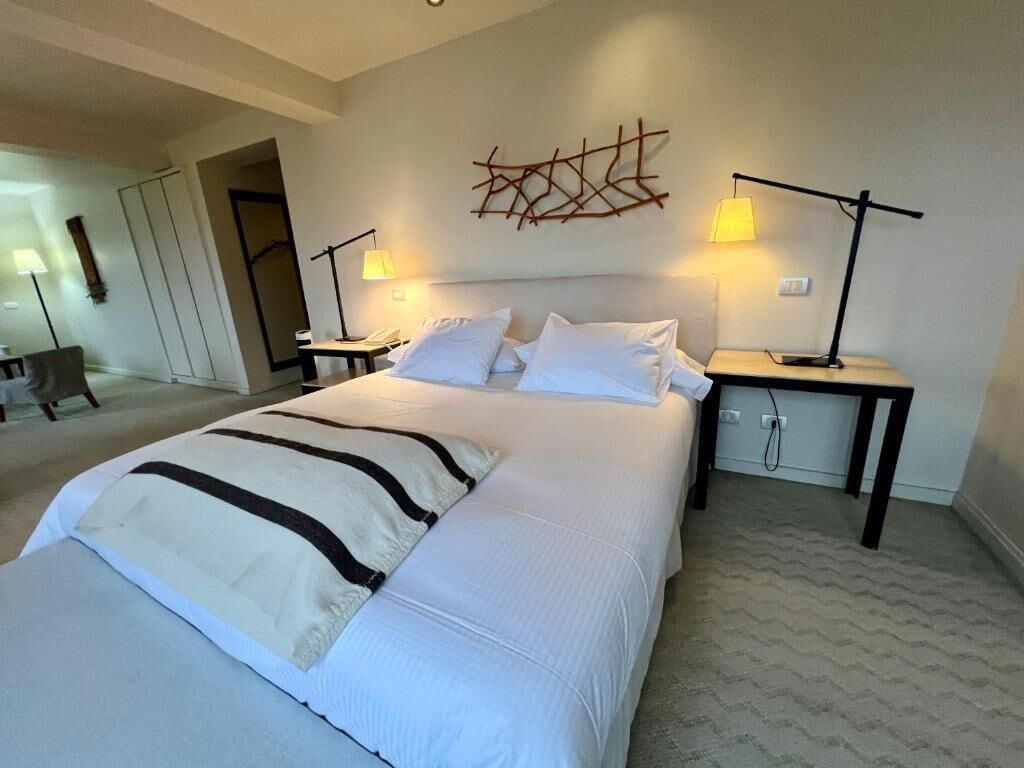 Una habitación de hotel con una cama grande, dos mesitas de noche, una obra de arte abstracto en la pared y una silla al fondo.