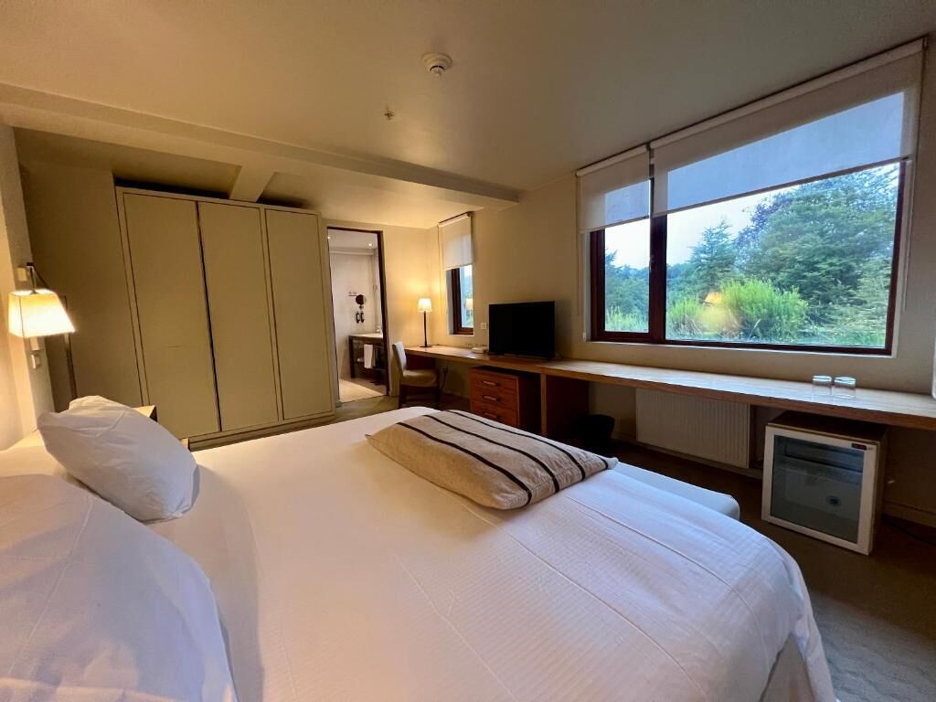Habitación de hotel con cama, escritorio, televisión y ventana con vistas a zonas verdes.