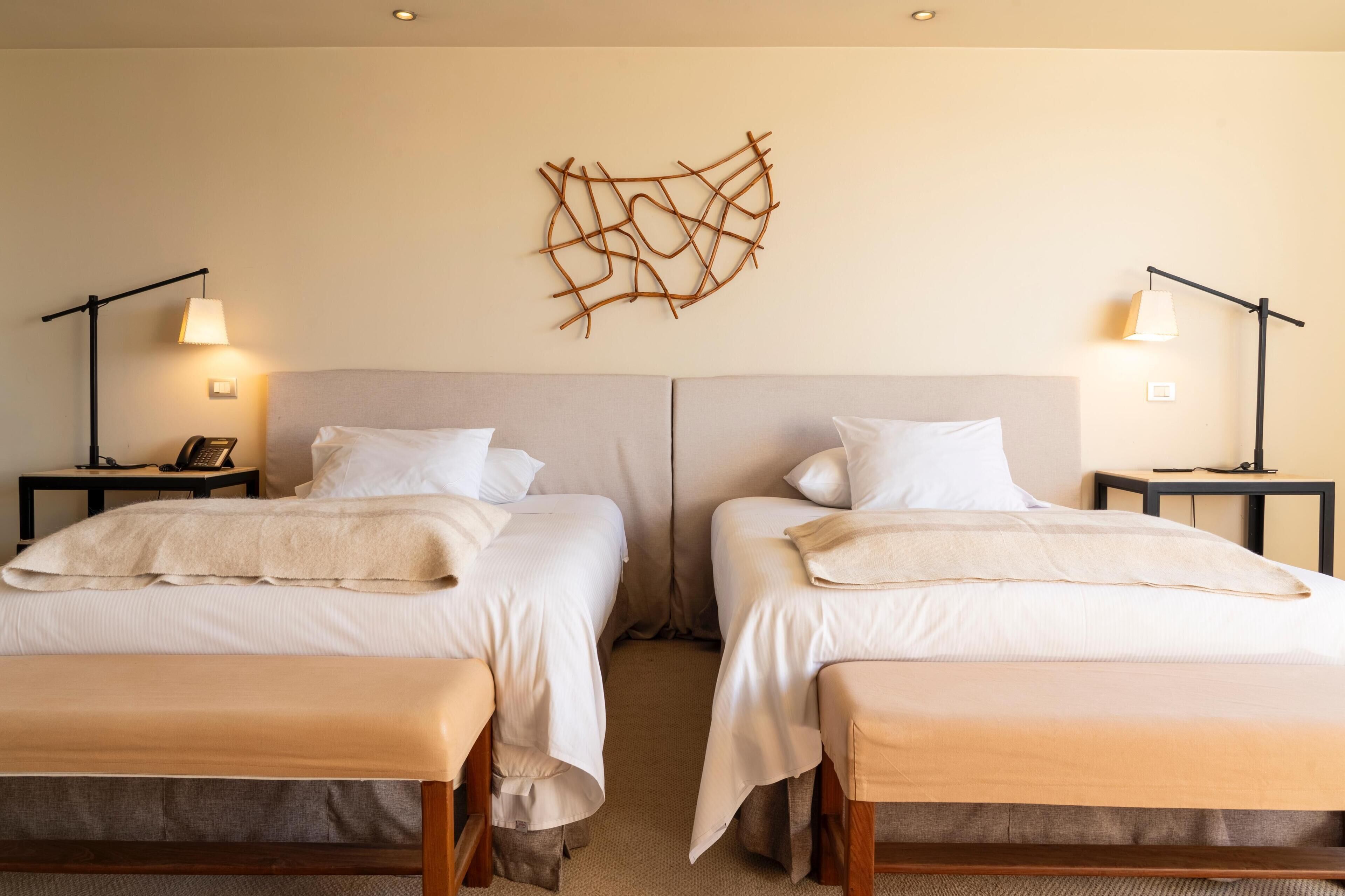 A hotel room with two beds, a wall-mounted abstract art piece, bedside lamps, and a telephone on the nightstand.