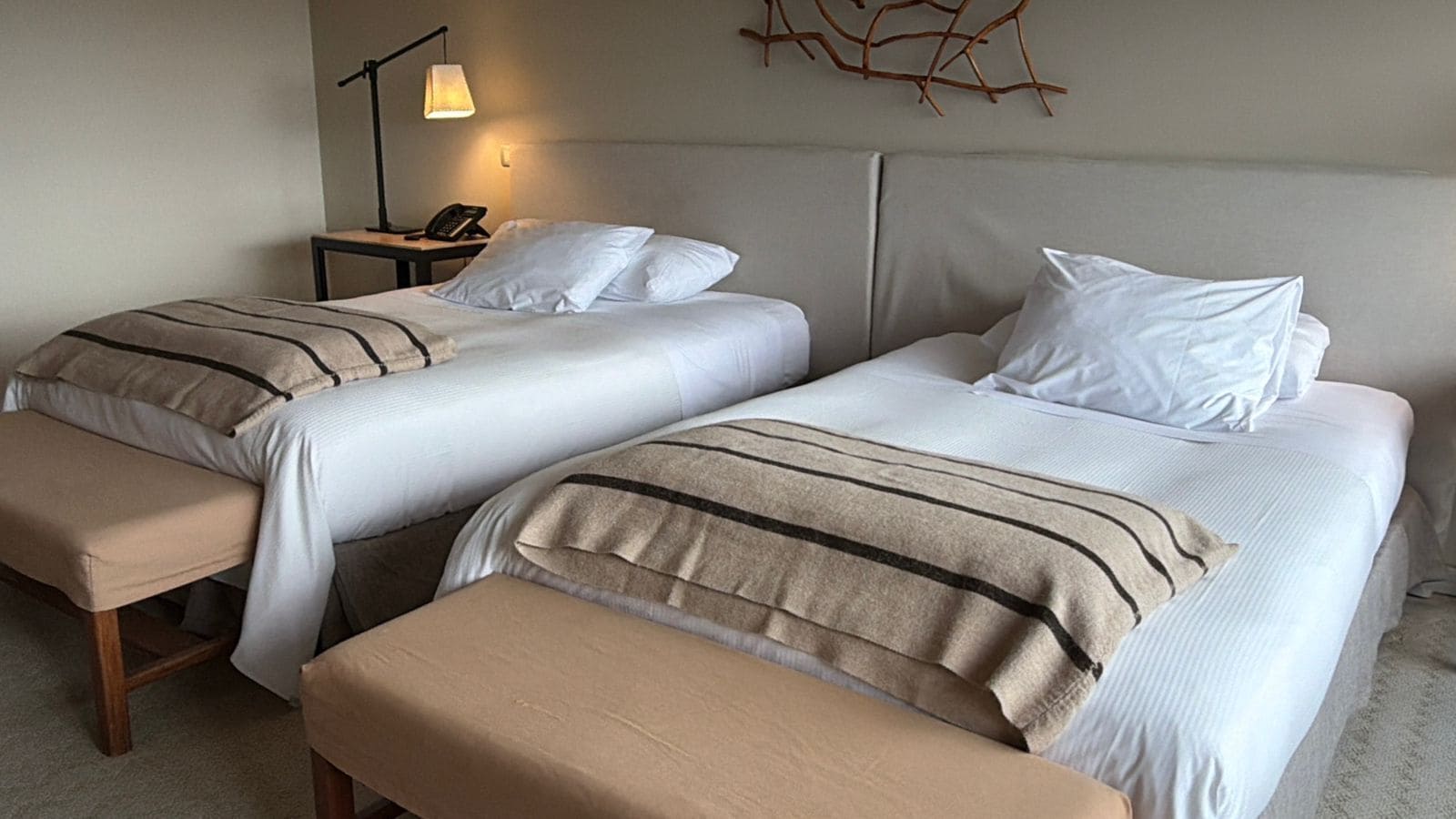 Une chambre d’hôtel avec deux lits, une table de chevet avec une lampe et un élément décoratif fixé au mur.