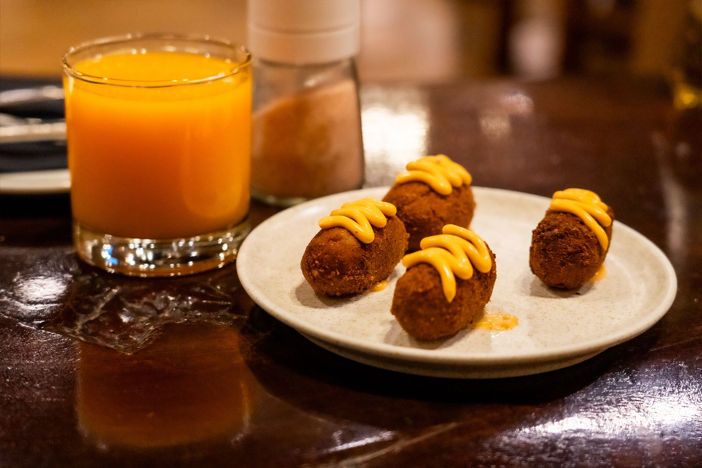 A plate of croquettes with a side of orange juice and condiments on a table.