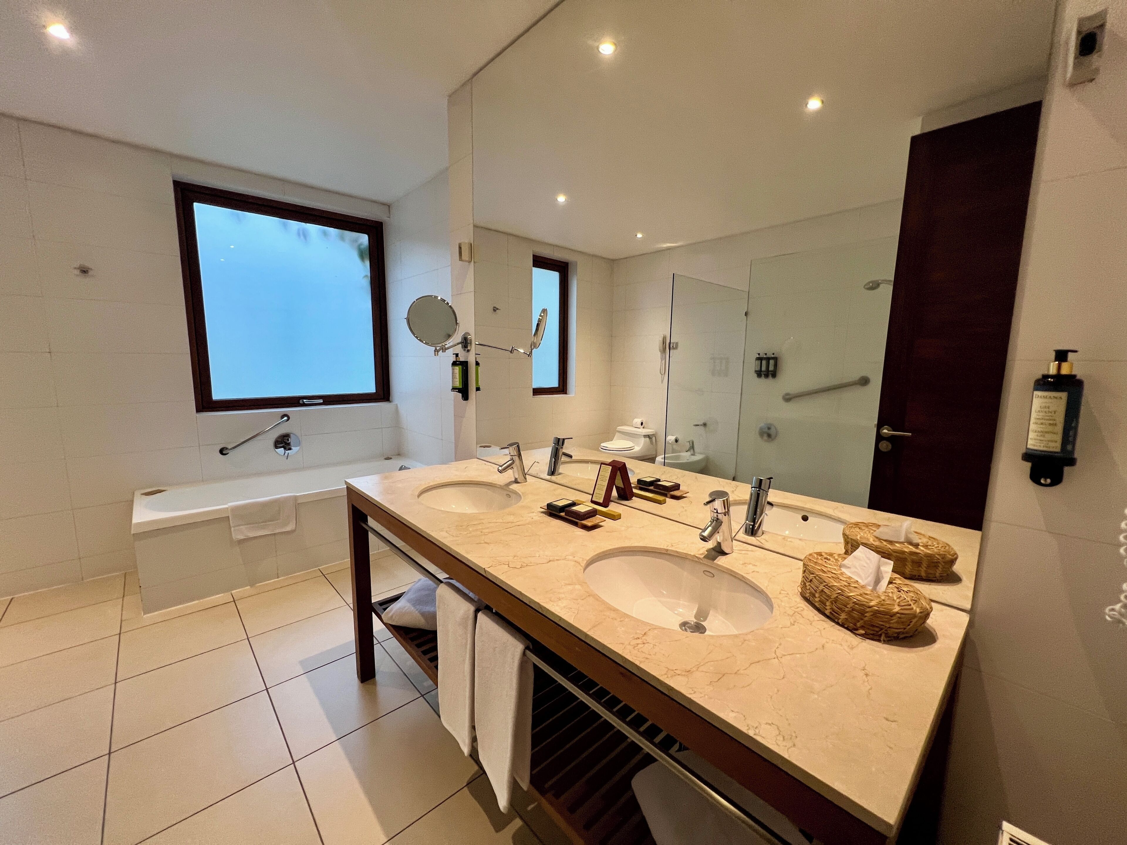 A modern bathroom with two sinks, a large mirror, and a window.