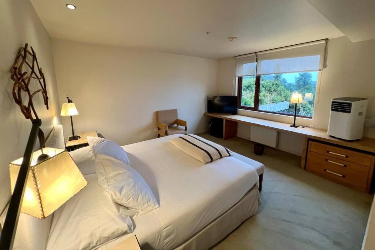 Ein Schlafzimmer mit Bett, Nachttischlampe, Schreibtisch, Stuhl und Fenster.