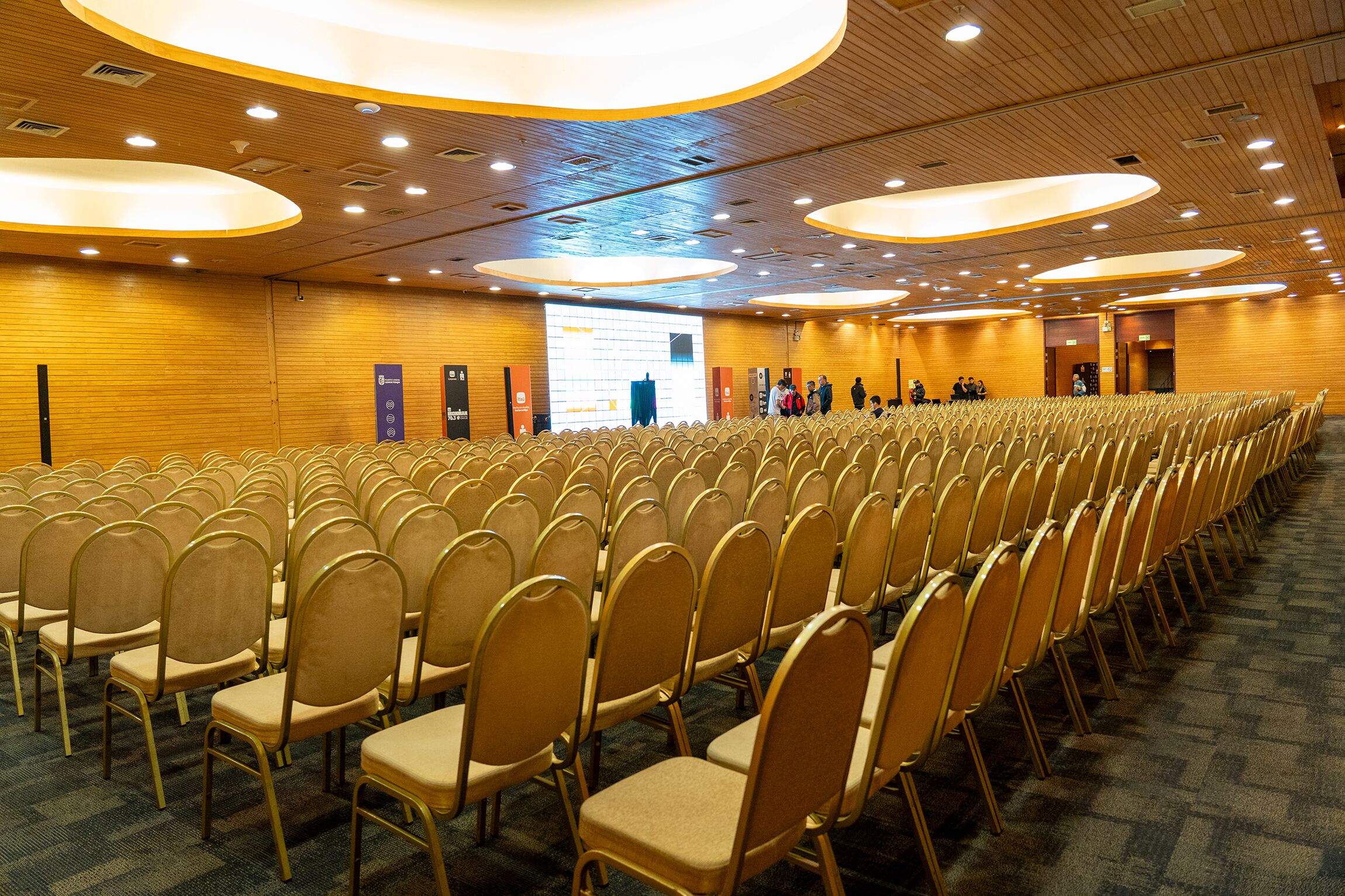 Ein Konferenzraum mit Reihen von Stühlen, Holzvertäfelung und Deckenleuchten.