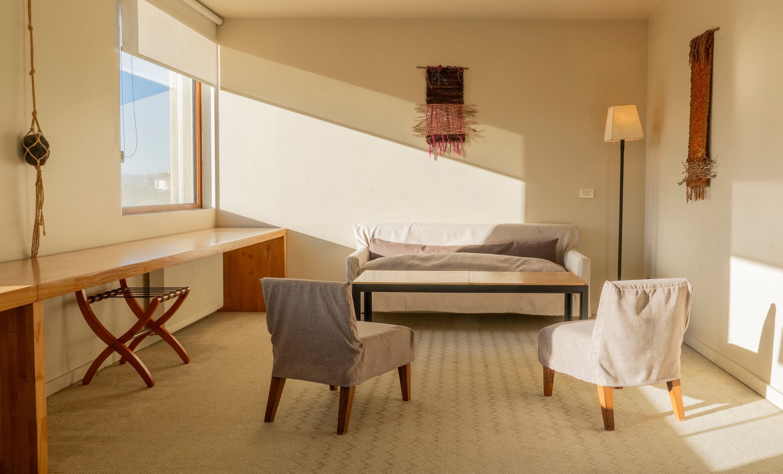 Ein Schlafzimmer mit einem Bett, zwei Stühlen, einem Schreibtisch, einer Wandtextil und einer Stehlampe.
