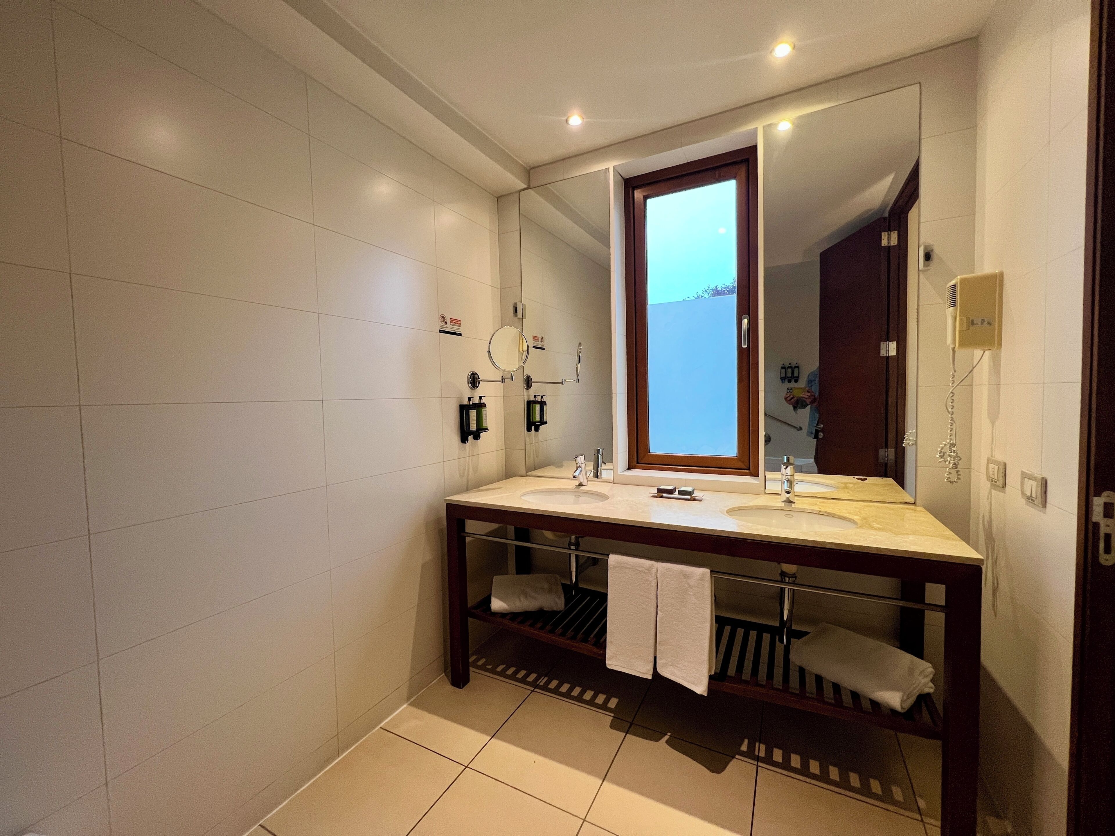 Un baño con un espejo grande, dos lavamanos, un perchero para toallas y una zona de ducha.