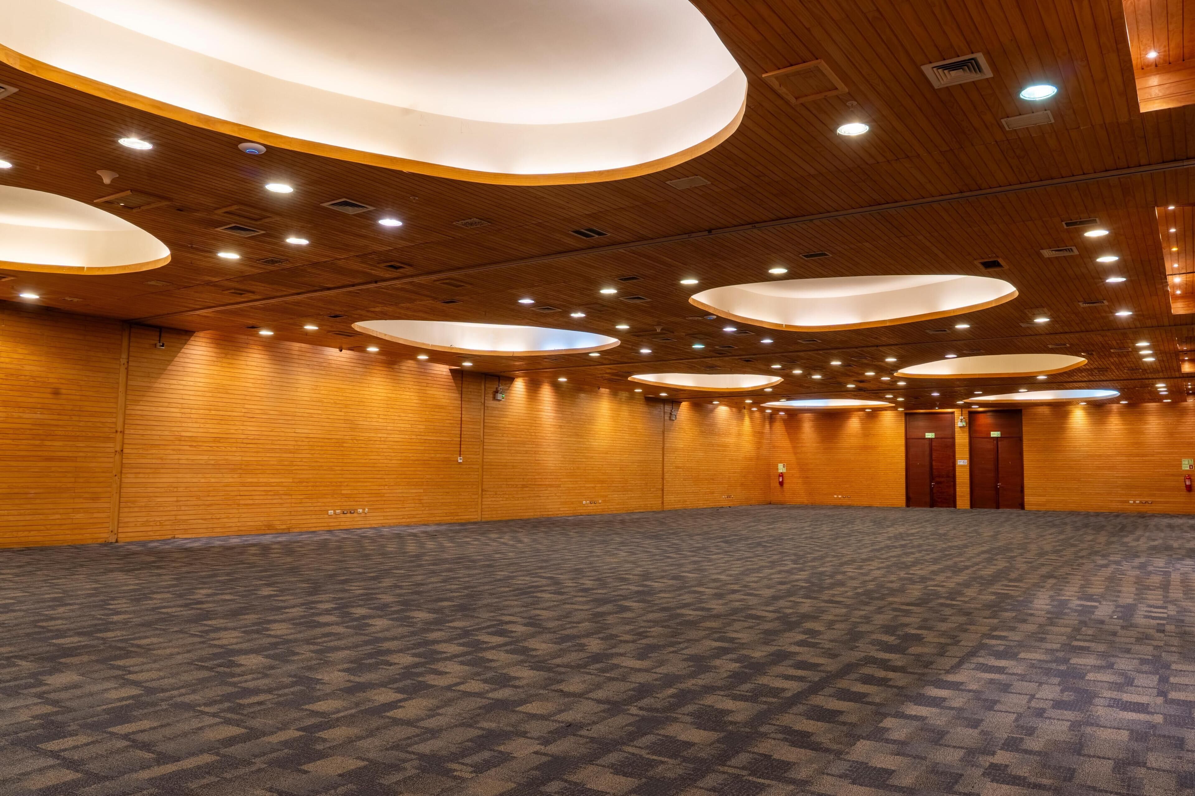 A spacious conference room with a patterned carpet, wooden panel walls, and circular ceiling lights.