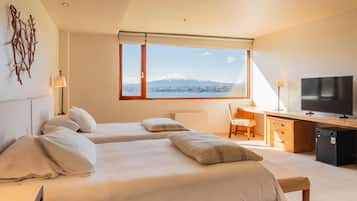 A hotel room with two beds, a desk, a chair, a TV, and a view of a mountain.