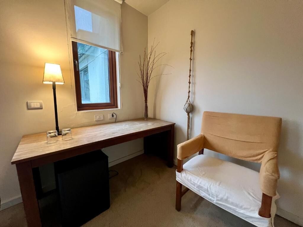 Ein Zimmer mit einem Holztisch, einem Stuhl, einer Lampe, einem Fenster und einer Zimmerpflanze.