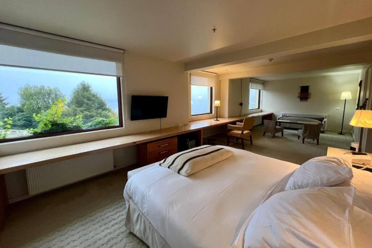 Ein Hotelzimmer mit einem großen Bett, einem Schreibtisch mit Computer, einem Fernseher und Blick ins Freie.