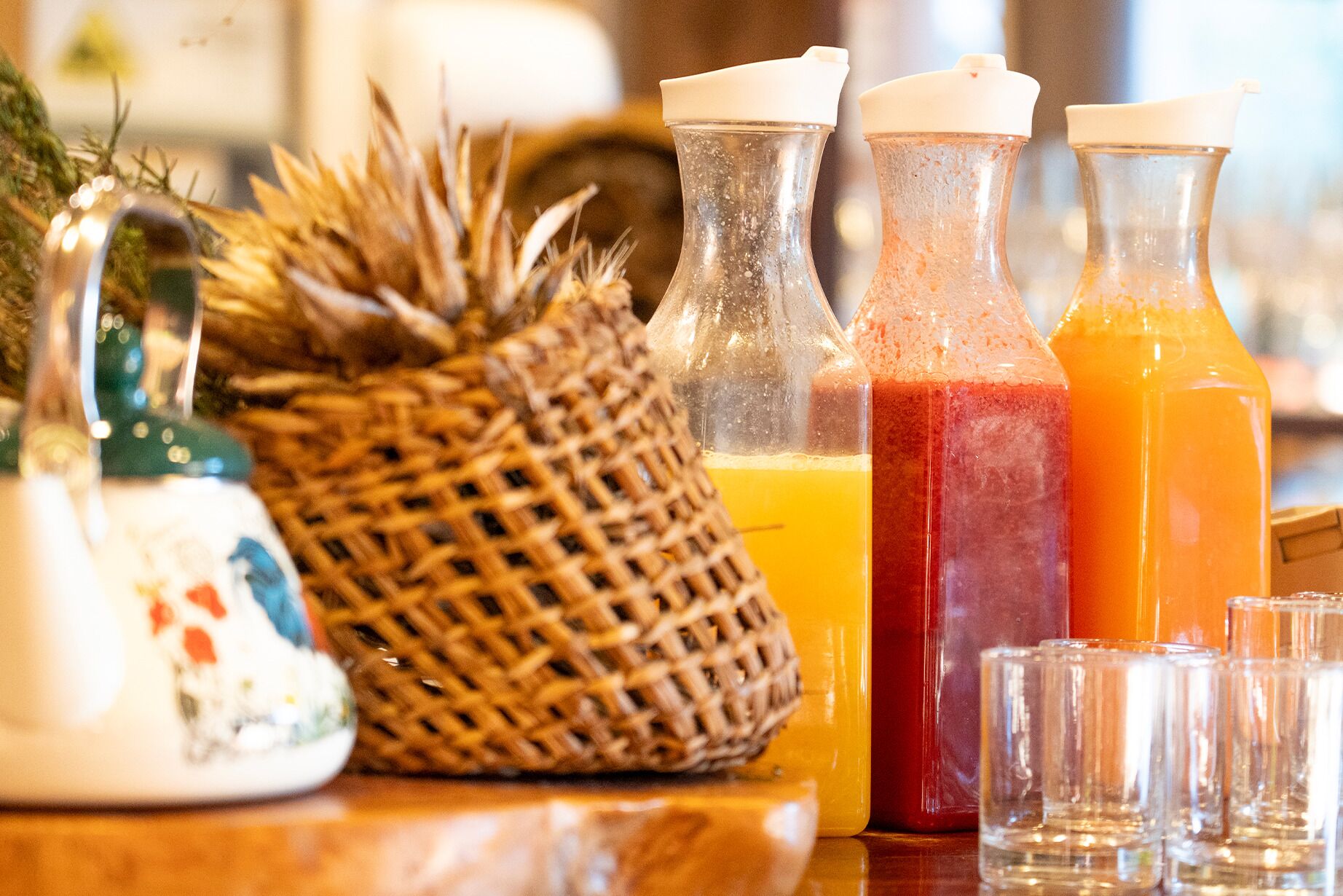A table with three glass bottles containing different colored liquids, a woven basket, and a decorative item.