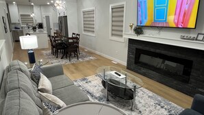 A modern living room with a fireplace, a dining area, and a kitchen in the background.