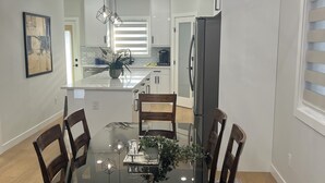 A modern kitchen with white cabinets, a stainless steel refrigerator, and a dining area with a glass table and wooden chairs.
